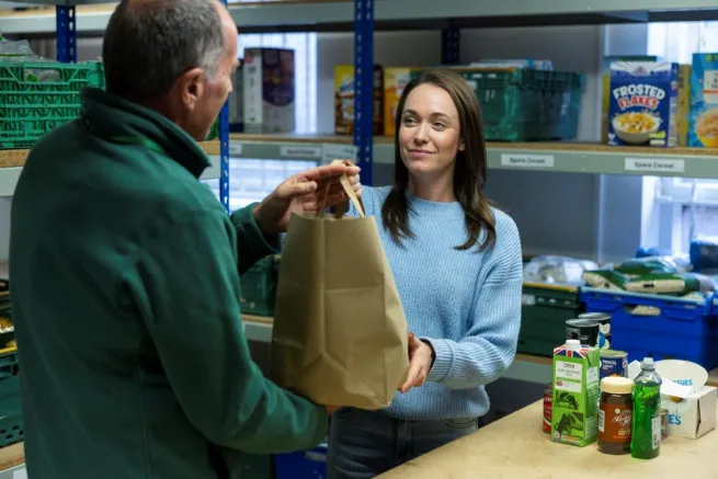 A food bank volunteer giving a food parcel to a woman in food bank