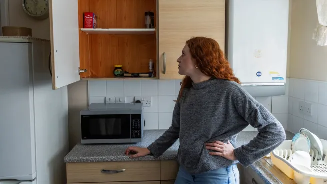 Woman standing in kitchen, looking at cupboard with hardly any food