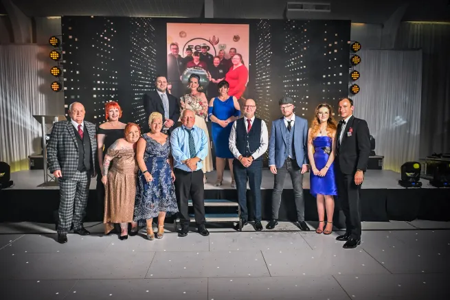Twelve people in formal clothing stand in front of stage