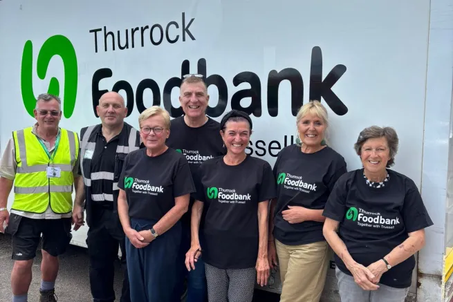 Seven volunteers wearing food bank t-shirts stand in front of food bank