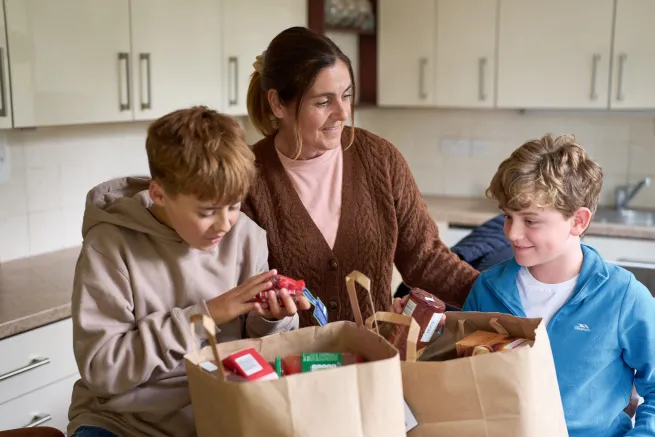 Mother and two sons unpack food parcel in kitchen