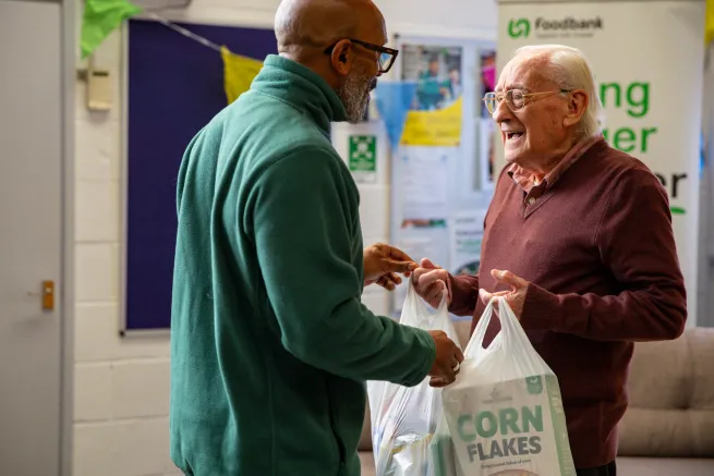 Volunteer giving food parcel to man in food bank