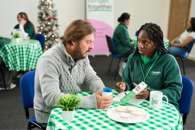Man sat at table with food bank volunteer looking at advice leaflet
