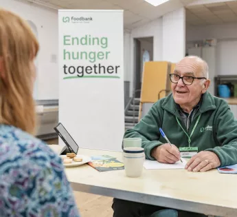 A volunteer speaking to a visitor at a table whilst filling in a form at the Cardiff food bank