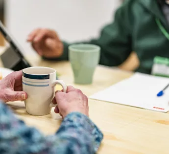 The hands of a foodbank volunteer and visitor at a table, with cups of tea.