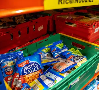 A crate of noodle packets stacked on a shelf a 'packet rice/noodle' over it