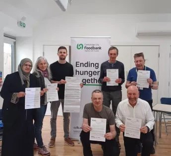 Seven people hold signed letters in front of a banner reading 'Ending hunger together'