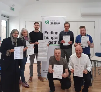Seven people pose around a banner reading 'Ending hunger together' holding letters.