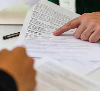 Two people at the table with a document, with someone pointing at a section