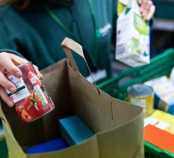 Hands of a volunteer placing a tin of tomatoes into a food parcel