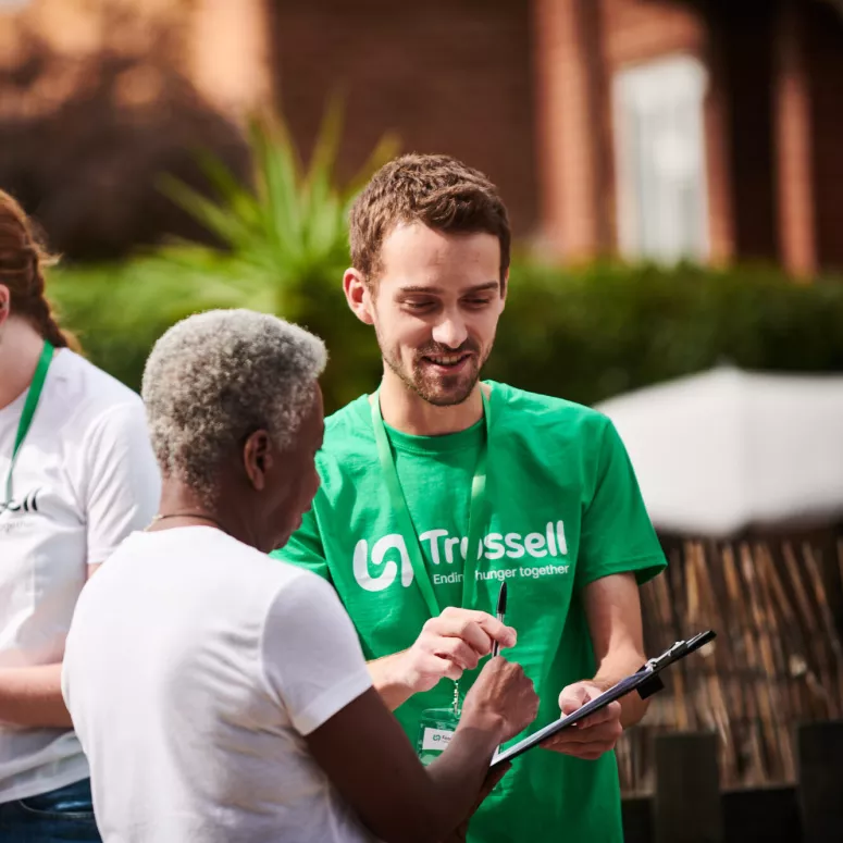 A woman signing a petition held by a man wearing a Trussell t-shirt