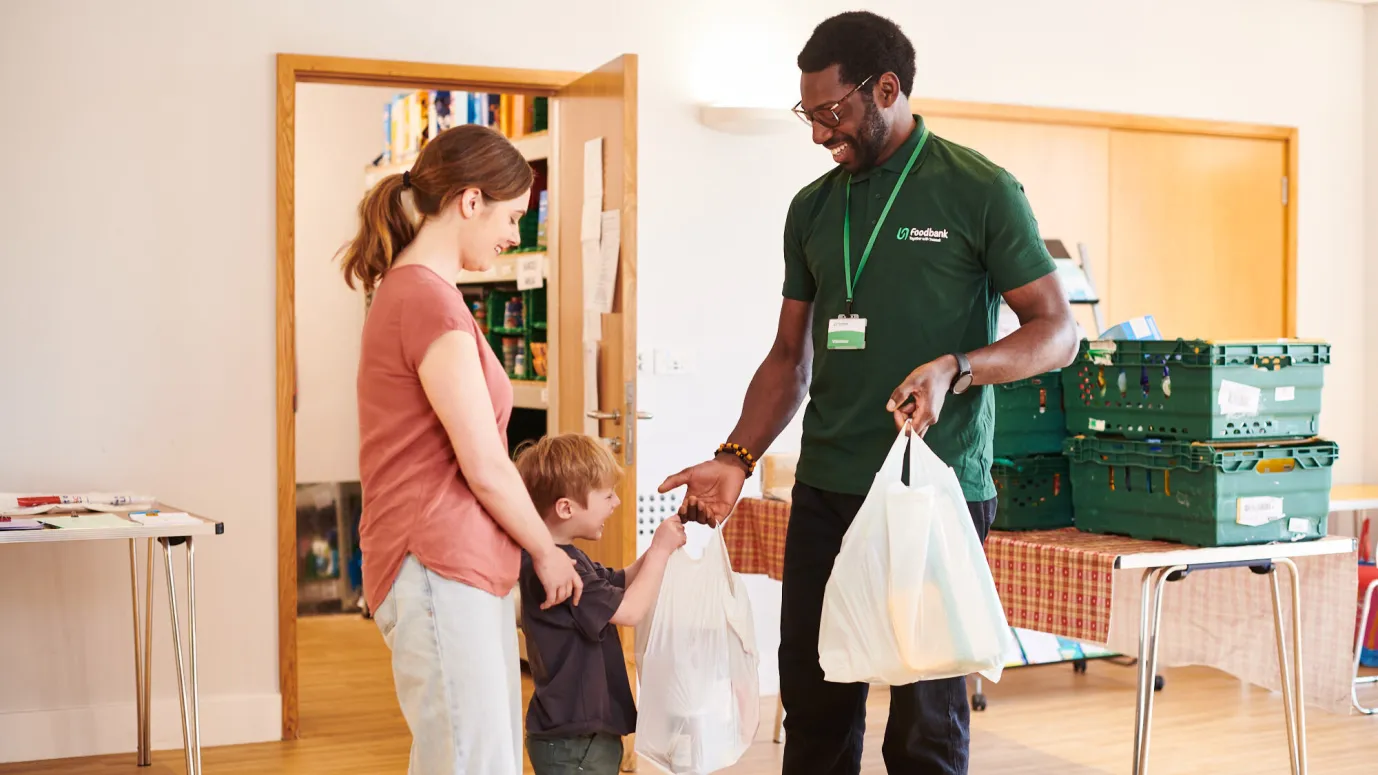 A volunteer hands Amy and Leo their food parcel at the food bank