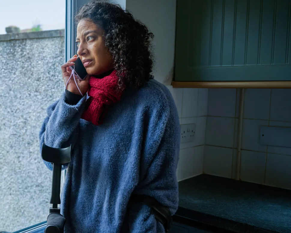 Woman on a mobile phone, in a kitchen, with crutches