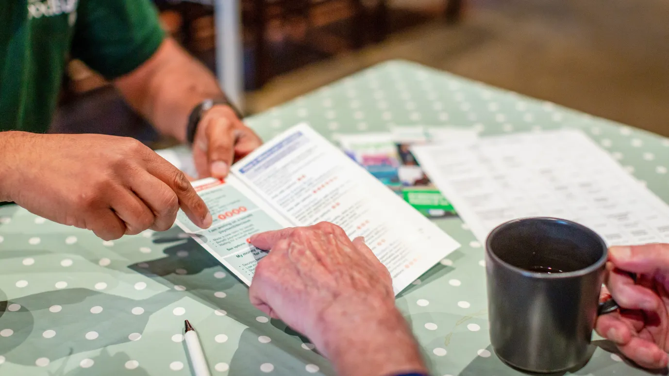 An individual with a cup of tea talking to a volunteer pointing at a leaflet
