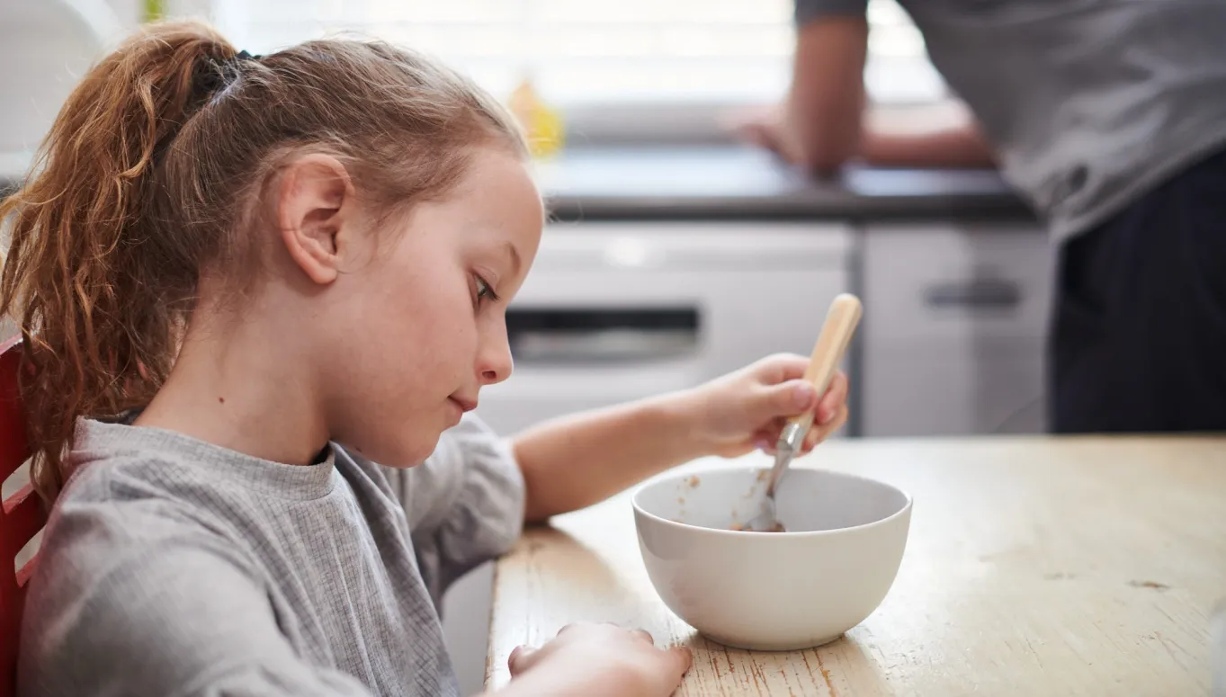 A young girl sitting down with an almost empty bowl of cereal