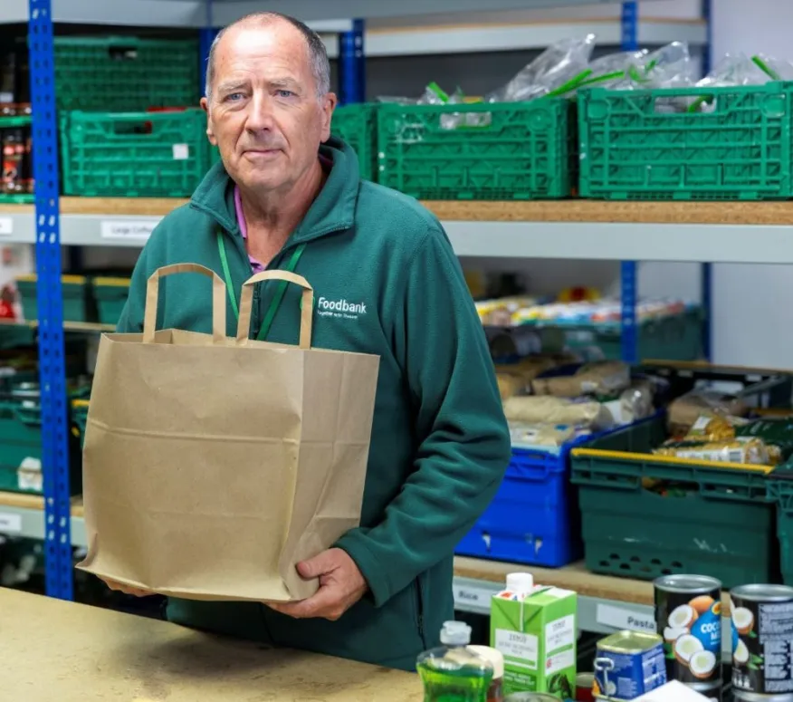 Food bank volunteer in warehouse, holding a food parcel