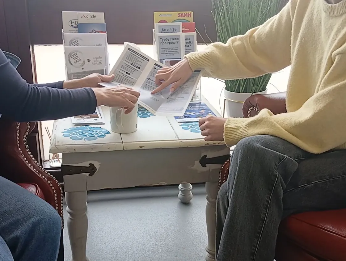 A person holding a leaflet out and an other person pointing to some text