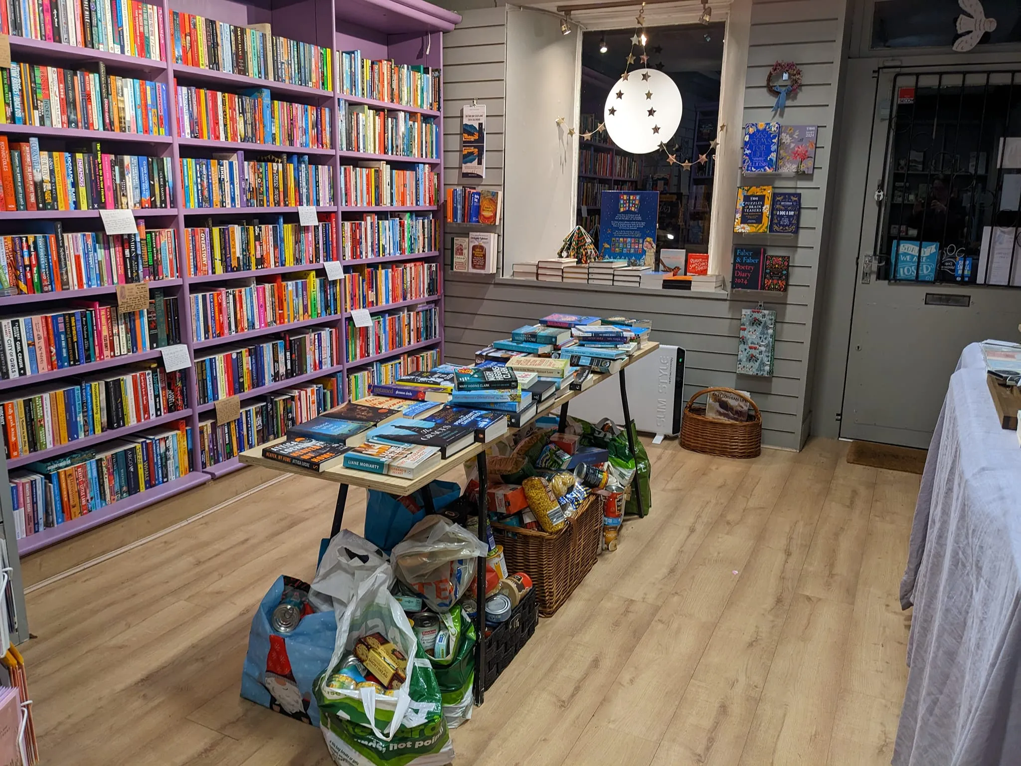 a book shop with a table in the centre with books on top and donations of food below the table.