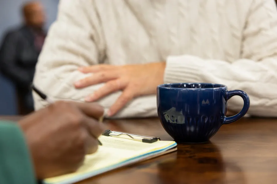 The hands of a food bank volunteer and visitor at a table, with cups of tea.