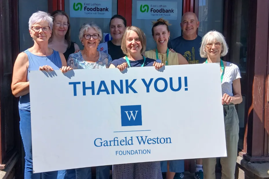 A group of people standing at the front doors of the foodbank holding up a thank you sign