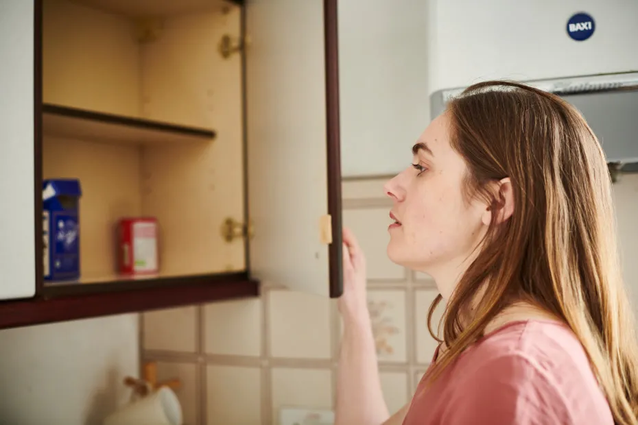 Woman looks into almost empty cupboard in her kitchen