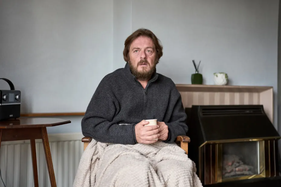Man sat on chair with blanket on lap holding a mug