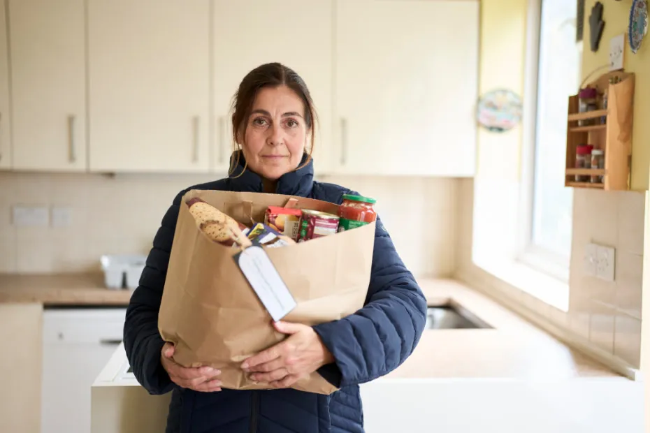 Woman standing in kitchen holding a bag full of food