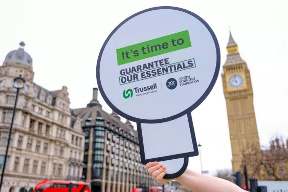 Guarantee our Essentials placard held against Big Ben backdrop
