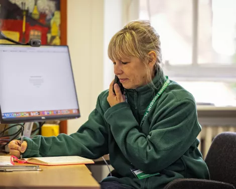 A Trussell volunteer sits at a desk, speaking on the phone while writing notes.