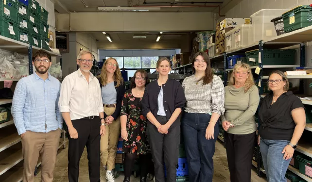 Eight people pictured in a warehouse full of food crates smiling and looking at the camera.