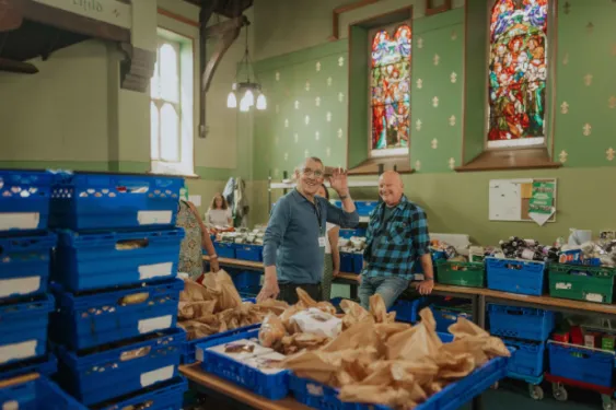 Two male volunteers smiling at the camera, one is waving