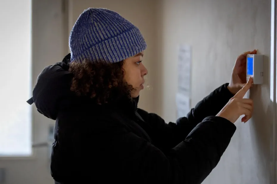 Woman wearing a hat and coat indoors, looking at thermostat