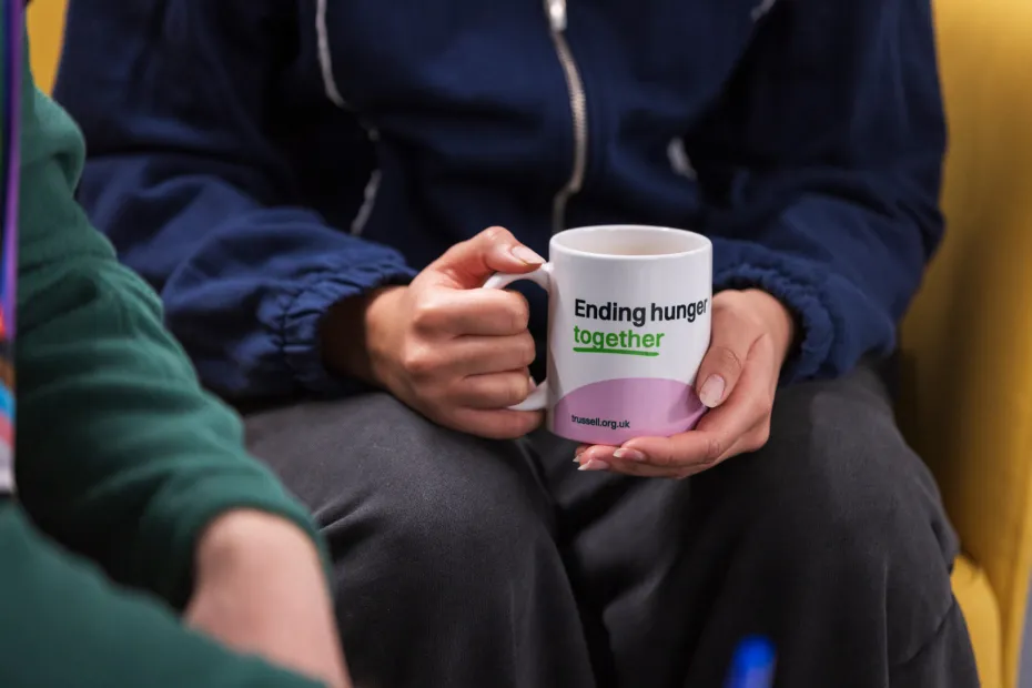 Food bank visitor sat holding a mug of tea with Ending hunger together written on mug