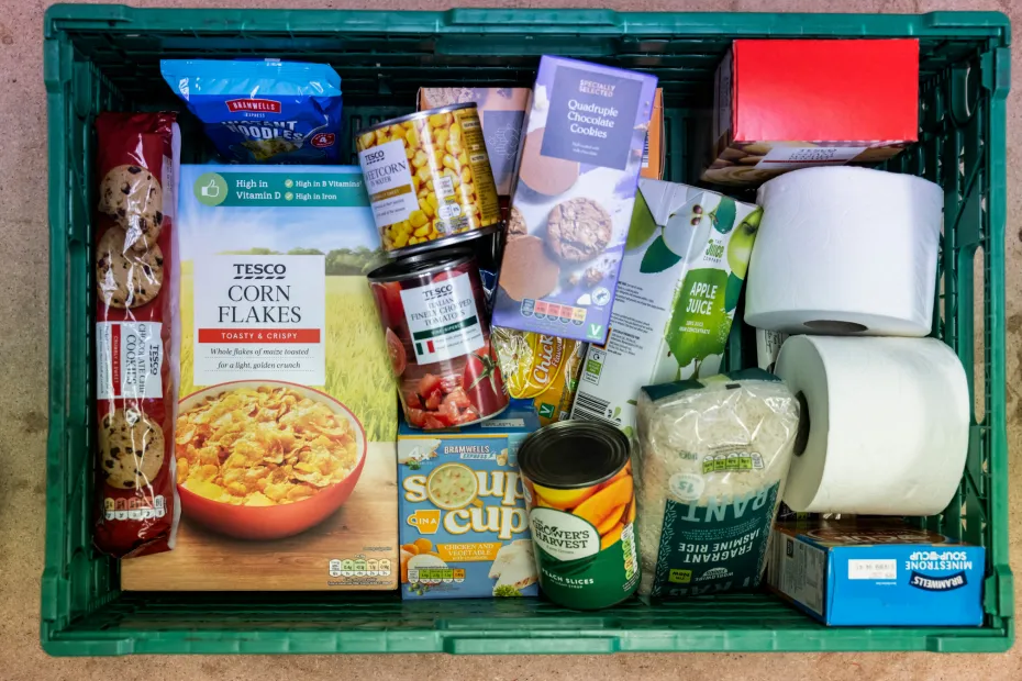 Green crate filled with a variety of items that make up a food parcel