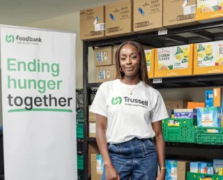 AJ Odudu, Trussell Ambassador, wearing a T-shirt with the Trussell logo standing next to a sign saying ending hunger together