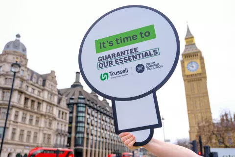 Guarantee our Essentials placard held against Big Ben backdrop