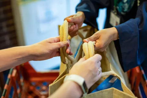 Two pairs of hands passing a shopping bag of food between them