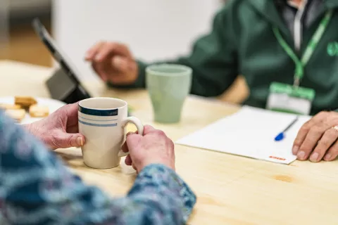 The hands of a foodbank volunteer and visitor at a table, with cups of tea.