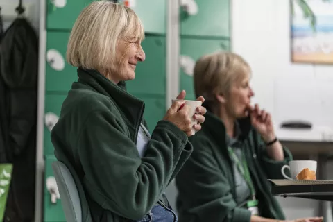 A smiling food bank volunteer holding a cup of tea.