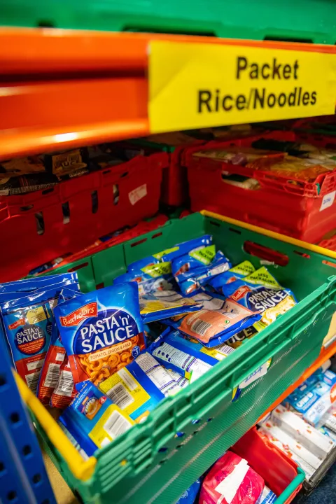 A crate of noodle packets stacked on a shelf a 'packet rice/noodle' over it