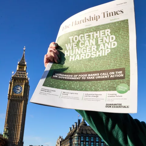 A copy of The Hardship Times is held up with Big Ben/The Elizabeth Tower in the background