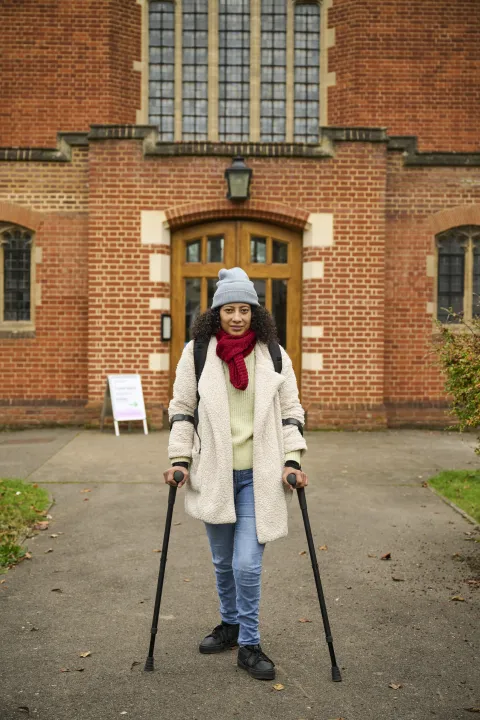A woman using crutches, bundled up in winter clothes, is walking out of a food bank.