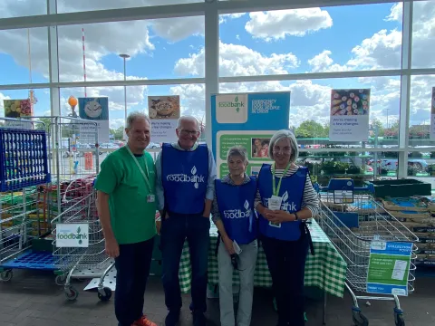 Four people wearing food bank t-shirts and holding a collection tin