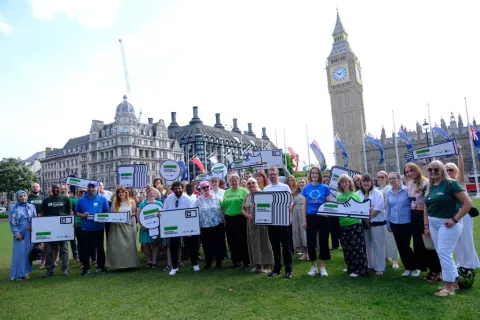 Group of people holding Essentials Guarantee placards with Houses of Parliament in the background