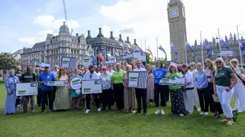 Large group of people holding Guarantee Our Essentials placards with Houses of Parliament in the background