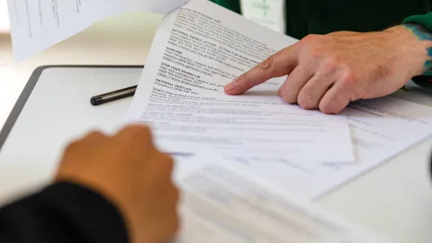 Two people at the table with a document, with someone pointing at a section