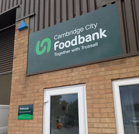Large dark green sign reading 'Cambridge City Foodbank' above a white door.