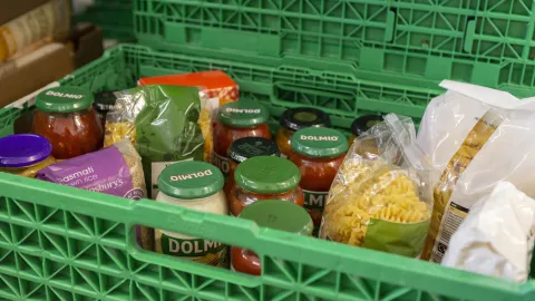 A close up of dried packets of pasta and jars of pasta sauces in a green crate