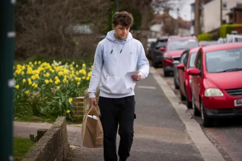 Young man walking along street carrying a food bank parcel