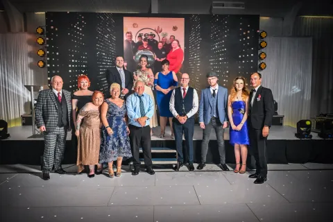 Twelve people in formal clothing stand in front of stage